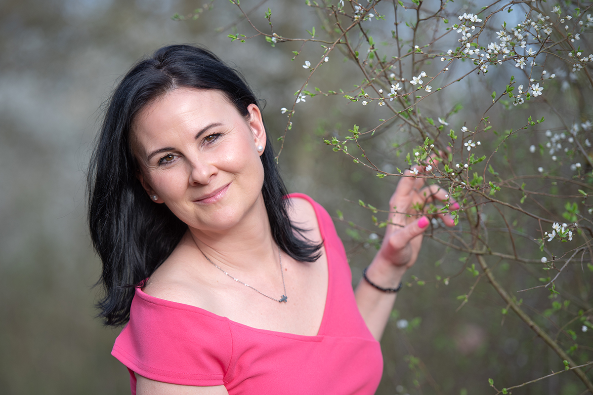 Žena v růžových šatech u rozkvetlého keře